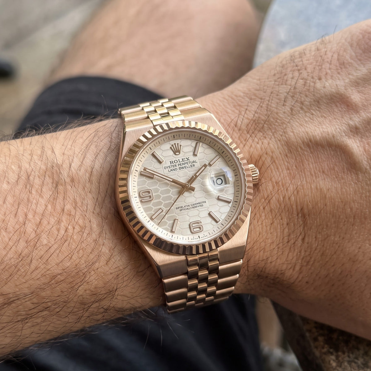 A close-up of a Rolex Day Date watch with a rose gold-tone metal bracelet and a white dial, worn on a person's wrist.